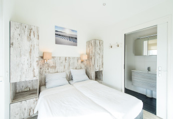Bright bedroom with two single beds, rustic wood cabinets and en suite bathroom at Boomhiemke, Netherlands.