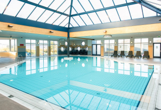 Piscina cubierta en un lodge, techos acristalados y tumbonas, con grandes ventanales dejando entrar luz solar.