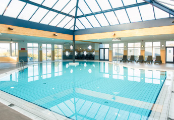 Piscina cubierta en un lodge, techos acristalados y tumbonas, con grandes ventanales dejando entrar luz solar.