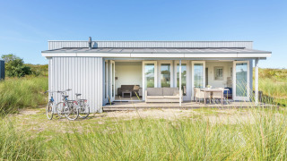 Holiday park Boomhiemke 7 lodge with veranda, bikes in front, and grassy surroundings under blue sky.