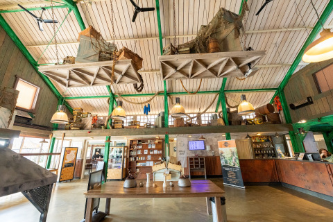 Innenansicht einer Lodge mit hoher Decke, hängenden Dekorationen und Rezeption im Erdgeschoss.