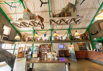 Vista interior de un lodge con techo alto, decoraciones colgantes y área de recepción en la planta baja.
