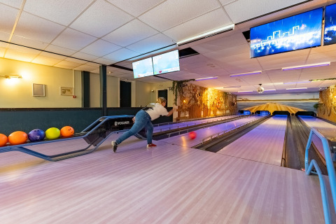 Person bowling on a lane in a lodge, colorful bowling balls to the left, warm and cozy lighting.