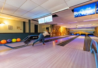 Person bowler på en bane i en lodge, med kugler i forskellige farver og stemningsfuld belysning.