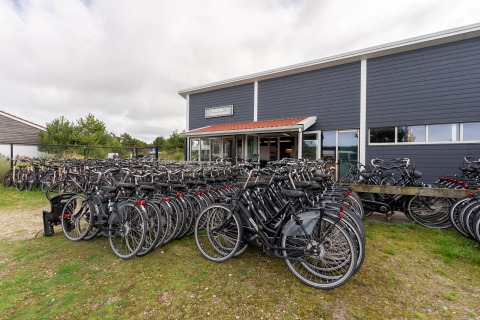 Viele Fahrräder stehen vor einer modernen Lodge mit grauer Fassade, geeignet für Radverleih.