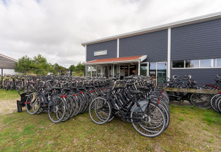 Numerose biciclette parcheggiate davanti a un moderno lodge, perfetto per gruppi e noleggio bici.