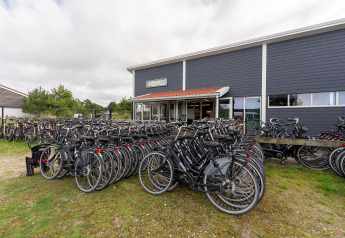 Cykler parkeret foran en lodge med mørke facade, himmel overskyet, cykeludlejning i Danmark.