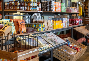 Butik i en lodge med hylder fyldt med snacks, te, marmelade, chips og aviser i trækasser.
