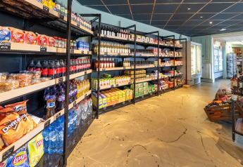 Hyggeligt butiksmiljø i en lodge med snacks, sodavand, vandflasker og forskellige dagligvarer på hylder.