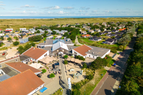 Vista aérea de un albergue con techos rojos, rodeado de casas del campo y dunas cerca de la costa.
