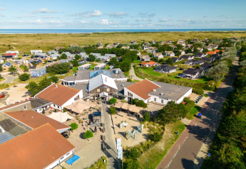 Luftfoto af en lodge med røde tage og omkringliggende hytter ved kysten og grønne områder i Danmark.
