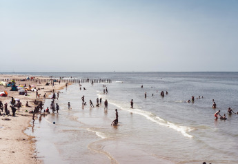 Folk nyder en solrig dag på stranden med børn, svømning og sandleg tæt ved vandkanten.