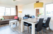 Lyst stueområde i Holiday park «Boomhiemke 6» i Holland med sofa, spisebord og store vinduer.