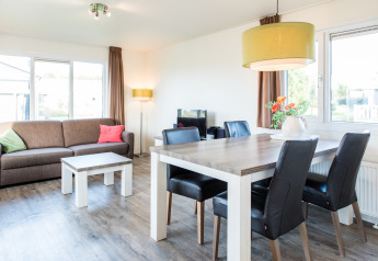 Lyst stueområde i Holiday park «Boomhiemke 6» i Holland med sofa, spisebord og store vinduer.