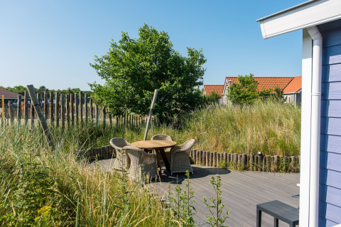 Terrasse mit geflochtenen Stühlen und Holztisch im Holiday Park Boomhiemke 6, Niederlande, im Grünen.