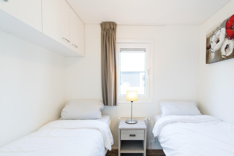 Habitación con dos camas individuales, ropa de cama blanca, mesita, lámpara y ventana en Holiday park Boomhiemke 6, Países Bajos.