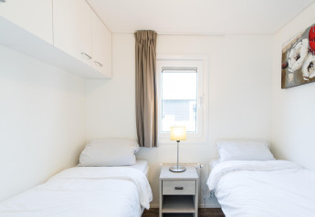 Habitación con dos camas individuales, ropa de cama blanca, mesita, lámpara y ventana en Holiday park Boomhiemke 6, Países Bajos.