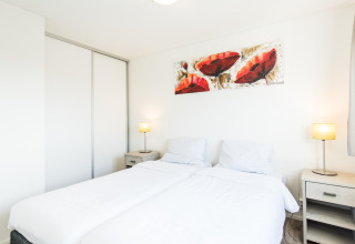Bright, modern bedroom with double bed, artwork and lamps at Holiday park «Boomhiemke 6» in the Netherlands.