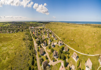 Luftfoto af ferieparken Boomhiemke 6 i Holland med hytter, grønne marker og havet i baggrunden.
