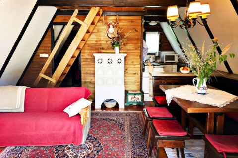Hyggelig lodgeindretning med skrå vægge, trævægge, rød sofa, spisebord og stige til hems i Østrig.