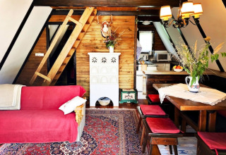 Hyggelig lodgeindretning med skrå vægge, trævægge, rød sofa, spisebord og stige til hems i Østrig.