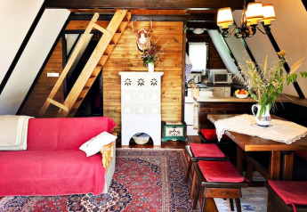 Hyggelig lodgeindretning med skrå vægge, trævægge, rød sofa, spisebord og stige til hems i Østrig.