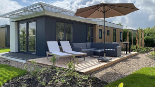 Terraza al aire libre en Zonneweelde Lodge, Camping Zonneweelde, Países Bajos, con tumbonas, sofá y sombrilla.