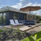 Udendørs terrasse ved Zonneweelde Lodge på Camping Zonneweelde i Holland med liggestole, sofa og parasol.