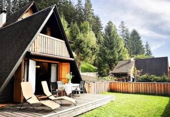 A-frame cabin at Ferienhütte Trabochersee in Austria with deck, sun chairs, and a grassy yard.