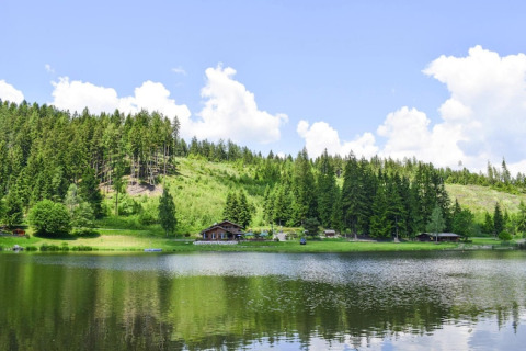 Scenisk udsigt over Ferienhütte Trabochersee ved en sø omgivet af skov og bjerge i Østrig.