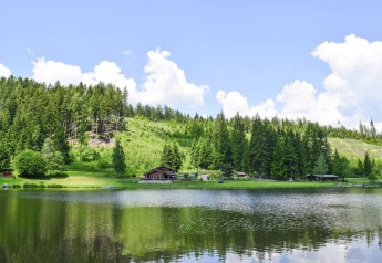 Vista panorámica del Ferienhütte Trabochersee junto a un lago tranquilo, rodeado de bosques y colinas en Austria.