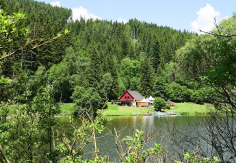 Zicht op de Ferienhütte Trabochersee-lodge aan een meer, omringd door bos in Oostenrijk op een zonnige dag.
