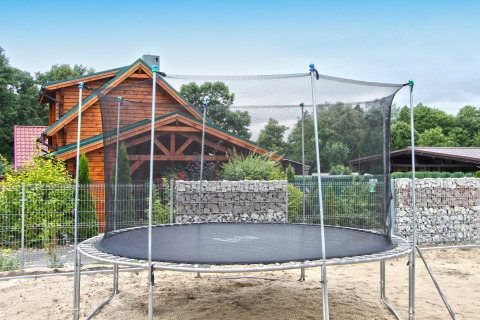 Stor trampolin med sikkerhedsnet i en have foran et træchalet, Holiday home «Maryna», Tyskland.