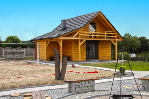 Holiday home Maryna : chalet en bois avec balcon, terrain de sable et foyer extérieur sous ciel bleu.