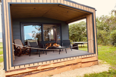 Wooden holiday chalet with covered porch, seating, hammock, and a dog relaxing in Nowe Warpno, Germany.