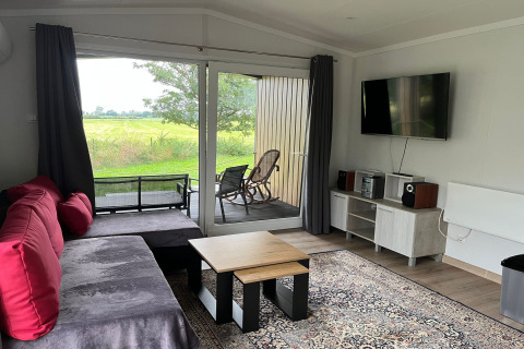 Living room in Holiday home Inselblick in Nowe Warpno, Germany, with sofa, TV, carpet and outdoor view.