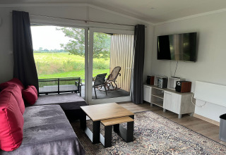 Living room in Holiday home Inselblick in Nowe Warpno, Germany, with sofa, TV, carpet and outdoor view.