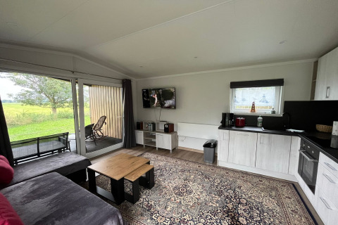 Living area of a holiday chalet in Nowe Warpno, Germany, with modern decor and garden view through glass doors.