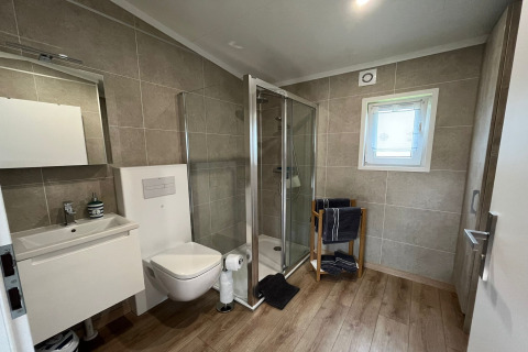 Modern bathroom in a German holiday chalet featuring a shower, wall-mounted toilet, sink, and window.