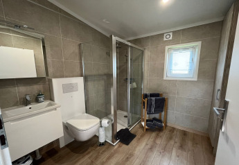 Moderne badkamer in een Duits vakantiehuis met douche, hangtoilet, wastafel en raam.