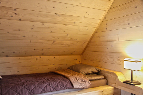 Gemütliches Einzelbett mit Holzwänden und Lampe im Dachzimmer des Holiday home «Maryna» in Deutschland.