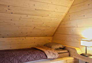 Letto accogliente con pareti in legno e lampada nella mansarda di Holiday home «Maryna» in Germania.