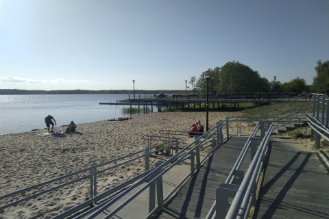 Sandy beach with boardwalk and people by the water at Holiday home «Inselblick in Nowe Warpno», Germany.