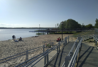 Sandy beach with boardwalk and people by the water at Holiday home «Inselblick in Nowe Warpno», Germany.