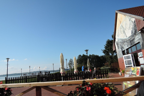 View from Holiday home Inselblick in Nowe Warpno, Germany, showing terrace seating, lake, and blue sky.