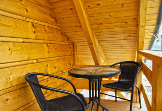 Træveranda med to sorte stole og et rundt bord på Holiday home «Maryna» chalet i Tyskland, solrig dag.