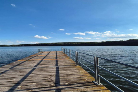 Holzsteg am See beim Ferienhaus «Maryna» in Deutschland, umgeben von Wasser und bewaldeten Hügeln.