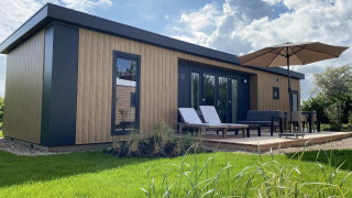 Exterieur van Zonneweelde Lodge Deluxe met modern houtdesign, ligstoelen en terras met grote parasol.