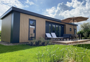 Esterno della Zonneweelde Lodge Deluxe, design moderno in legno, lettini e terrazza con grande ombrellone.