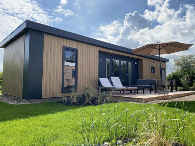 Exterior de la Zonneweelde Lodge Deluxe con diseño moderno de madera, tumbonas y terraza con sombrilla grande.